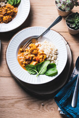 Chickpea and cauliflower vegetarian curry with brown rice and spinach on a wooden table.