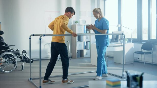 Hospital Physical Therapy Room: Strong Patient with Injury Walking Holding for Parallel Bars, Physiotherapist Encourages Assists, Helps Disabled Person Do Rehabilitative Physiotherapy. Slow Motion