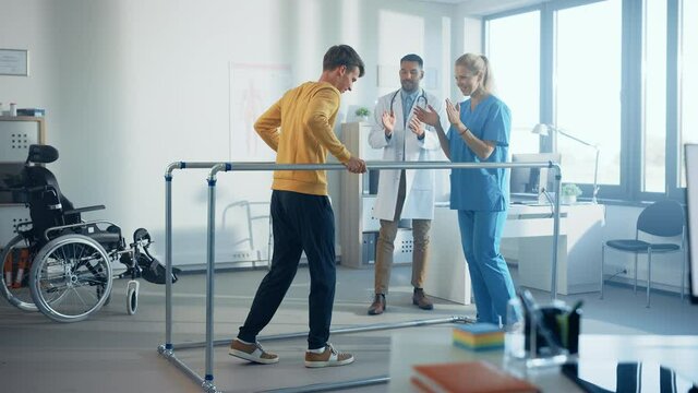 Hospital Physical Therapy: Strong Patient with Injury Making First Steps, Walks Holding for Parallel Bars. Physiotherapist, Rehabilitation Doctor Assist, Help Disabled Person. Side View Slow Motion
