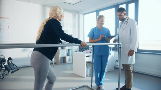 Hospital Physical Therapy: Strong Determined Senior Female Patient with Injury Walks on Treadmill Holding Parallel Bars. Physiotherapist, Rehabilitation Doctor Assist, Help Disabled Person to Heal