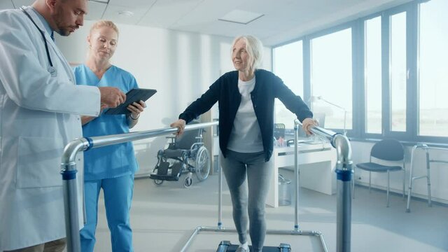 Hospital Physical Therapy: Strong Determined Senior Female Patient with Injury Walks on Treadmill Holding Parallel Bars. Physiotherapist, Rehabilitation Doctor Assist, Help Disabled Person to get Well
