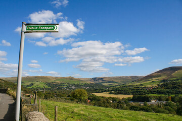 Mossley, England - A view of rolling hills on the outskirts of Mossley England, under a sign that says "public footpath", under an idyllic blue sky.  Image has copy space.