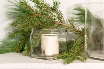 white candle decoration with green pine branches behind; wintergreens