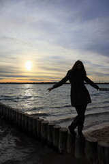 Fototapeta premium Silhouette einer jungen Frau, die bei Sonnenuntergang auf einer hölzernen Buhne am Markkleeberger See balanciert, Sonnenuntergang am Markleeberger See, bei Leipzig, Sachsen, Deutschland