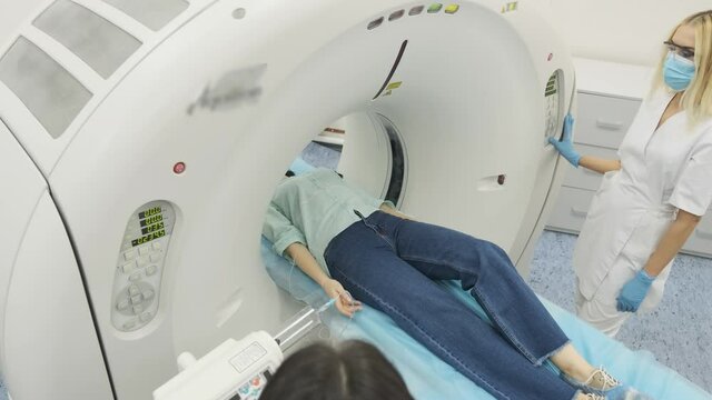 Female patient is undergoing CT or MRI scan under supervision of two qualified radiologists in mask and gloves in modern medical clinic. Patient lying on a CT or MRI scan table