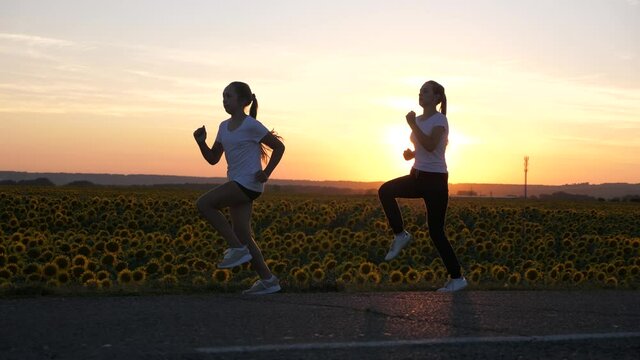 Warm up sports girls. Evening running workout. Sports teenagers run along road in glare of sunset. Healthy jogging and outdoor exercise concept. Girls jogging. Freedom, life in motion, health.