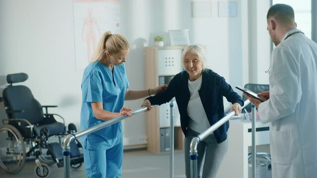 Hospital Physical Therapy: Portrait of Strong Senior Female Patient with Injury Successfully Walks Holding Parallel Bars. Physiotherapist, Rehabilitation Doctor, Help, Assist Disabled Patient