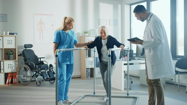 Hospital Physical Therapy: Portrait of Strong Senior Female Patient with Injury Successfully Walks Holding Parallel Bars. Physiotherapist, Rehabilitation Doctor, Help, Assist Disabled Patient