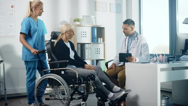 Hospital Physical Therapy: Strong Senior Female in Wheelchair, Talks to a Friendly Rehabilitation Physiotherapist Doctors Gives Advice, Plans Rehabilitation Treatment for Determined Disabled Patient