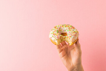 A child's hand with a nibbled donut on a light pink background.