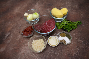 The ingredients for kharcho soup are laid out separately in bowls on a granite table. A piece of fresh raw beef, peeled potatoes, onions, rice, spices. Step by step recipe.