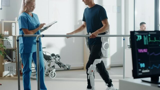 Modern Hospital Physical Therapy: Doctor Uses Tablet Computer, Helps Disabled Patient with Injury Walk on Treadmill Wearing Advanced Robotic Exoskeleton Legs. Physiotherapy Rehabilitation Technology