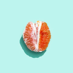 Bright grapefruit or red orange without peel on pastel turquoise background. Minimal fruit and summer concept.