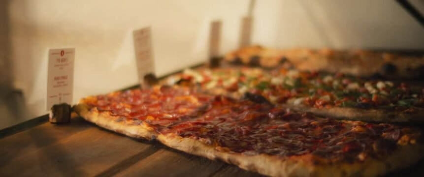 Delicious al taglio pizzas with different toppings being placed on a wooden surface in a pizza cafe.