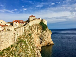 A view of a section of the walls of Dubrovnik facing outwards to the Adriatic Sea.  People are standing in the distance admiring the view.