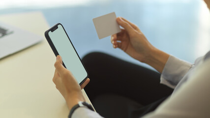 Side view of female holding smartphone and name card while working in office room