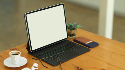 Cropped shot of wooden table with tablet, keyboard, eyeglasses, accessories and cup