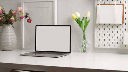 Home office desk with laptop, stationery, decorations and flower vase