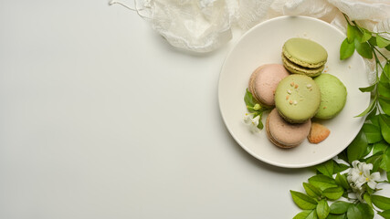 White table with a plate of French colourful macarons, copy space decorated with flower and leaves