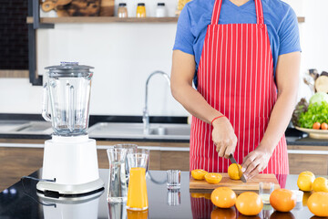 Healthy man is slicing fresh orange fruit to make juicing, orange juice in kitchen room at home