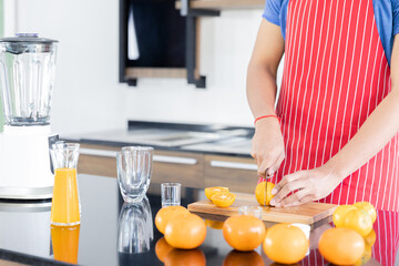 Healthy man is preparing orange and slicing to make  juicing, orange juice in kitchen room at home.