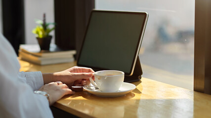Female hand relaxing with coffee cup on wooden bar with digital tablet in cafe