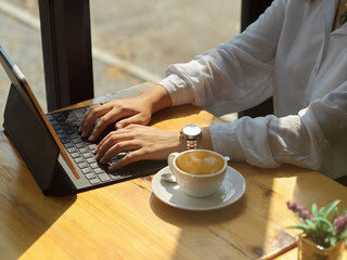 Fototapeta na wymiar Female hands typing on tablet keyboard on wooden table with coffee cup in cafe