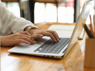 Female hands typing on laptop keyboard and working with stationery on the table