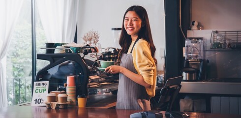 Fototapeta na wymiar Young Asian woman barista wear apron making coffee cup served to customer at bar counter in coffee shop with smile face.Concept of cafe and coffee shop small business.Vintage tone