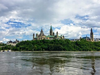 An amazing view of parliament hill surrounded by green forest and chateau laurier from the perspective of a tour boat on the Ottawa river.  This is beautiful view of the cityscape on a nice summer day