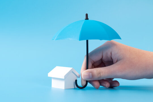 Home insurance or mortgage protection concept with a 3D house model under a blue umbrella