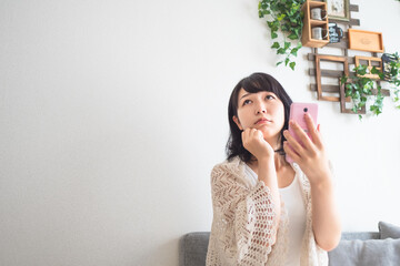 スマホを持ち不安げな表情の女性のイメージ