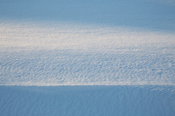 Beautiful winter background with snowy ground. Natural snow texture. Wind sculpted patterns on snow surface. Closeup top view with copy space.