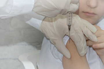 The doctor's hands in medical gloves are vaccinating a child, a boy, in the shoulder. The concept...