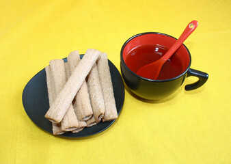 Morning cup of tea in a black and red mug, with waffle tubes with filling.