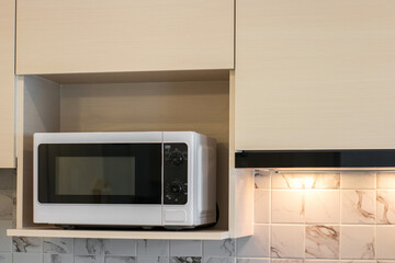 White microwave on a wooden shelf in kitchen at apartment