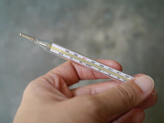 Hand held a close-up of a glass thermometer. Behind there is a picture of hand washing alcohol...