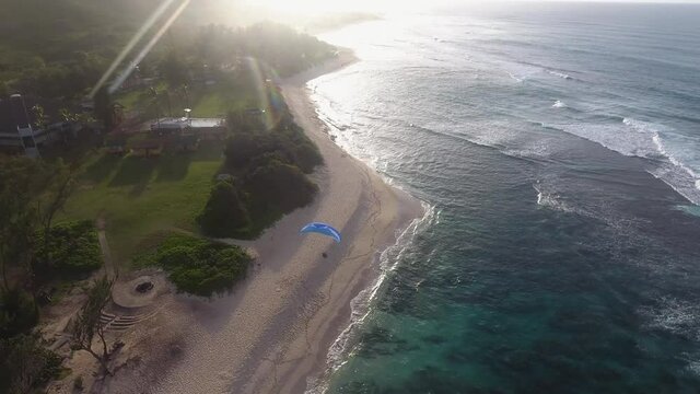 Aerial drone shot of parachuter flying over beach in hawaii during sunset