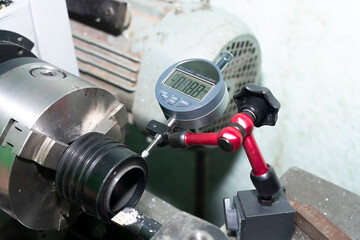 A digital micrometer checks the runout of a part in a lathe.