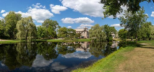 Panorama of Stewart Park, a view of the willow trees and stone house, surrounded by other trees,...