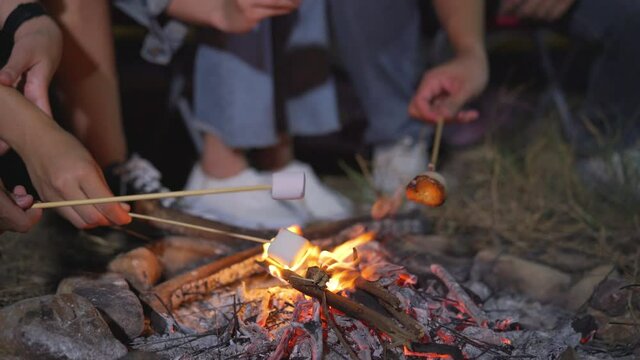 Close up hand group friends 
grill marshmallows and enjoying their time tent camping
