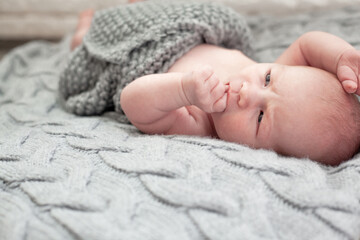 Cute baby lies on knitted grey blanket. New born baby smiling happily at camera. Care body concept