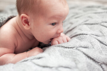 Cute baby lies on knitted grey blanket. New born baby smiling happily at camera. Care body concept