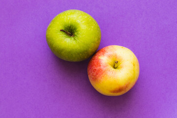 Green apple and yellow-red apple, on a purple background