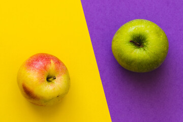 Green apple and yellow-red apple, on a half purple and half yellow background