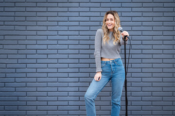 Young Blonde Female Comedian Against Blue Grey Brick Wall with Microphone and Expressions - Powered by Adobe