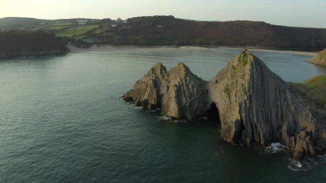 Smooth drone aerial shot of three cliffs bay with couple on the cliff in the Gower, Wales, surrounded by the sea