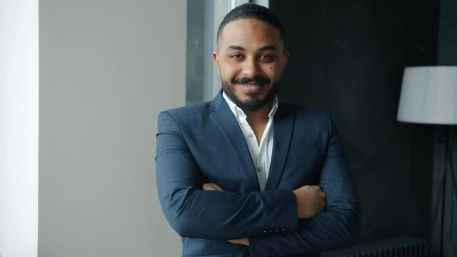 Slow motion of handsome Arab businessman in suit standing in office smiling looking at camera. Businesspeople and modern workplace interior concept.
