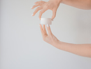 Plastic jar of cream in a female hand isolated on white. Professional cosmetics to restore skin youth, anti-aging cream. Skin care concept. Jar mockup.