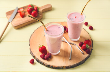 Glasses of tasty smoothie with strawberry and raspberry on light background